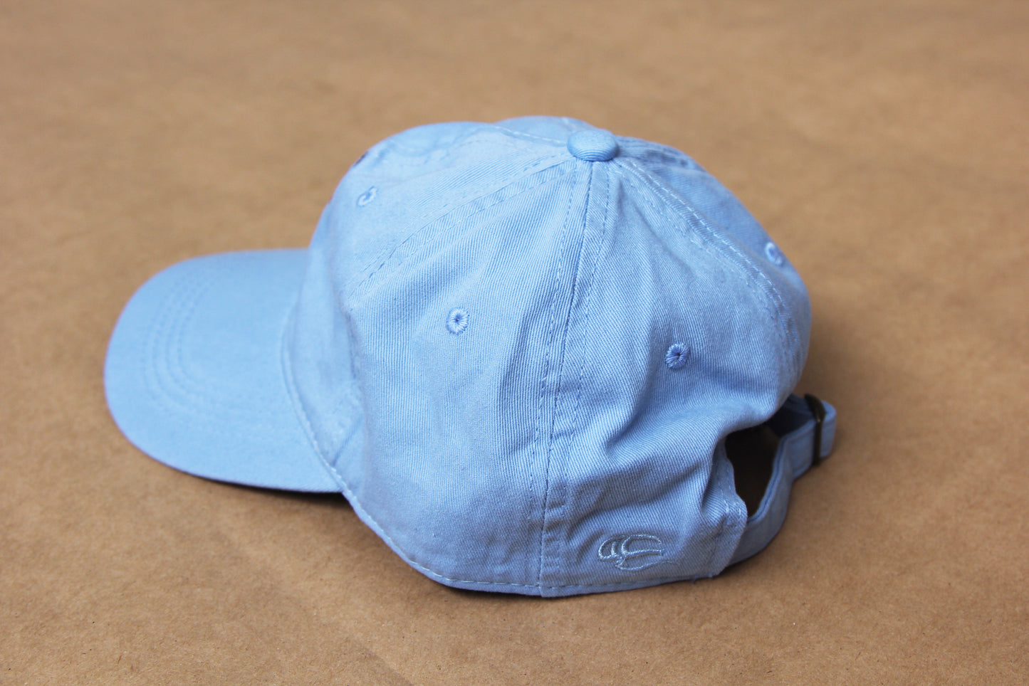 A photo of the back of a light blue colored dad hat over a tan background.