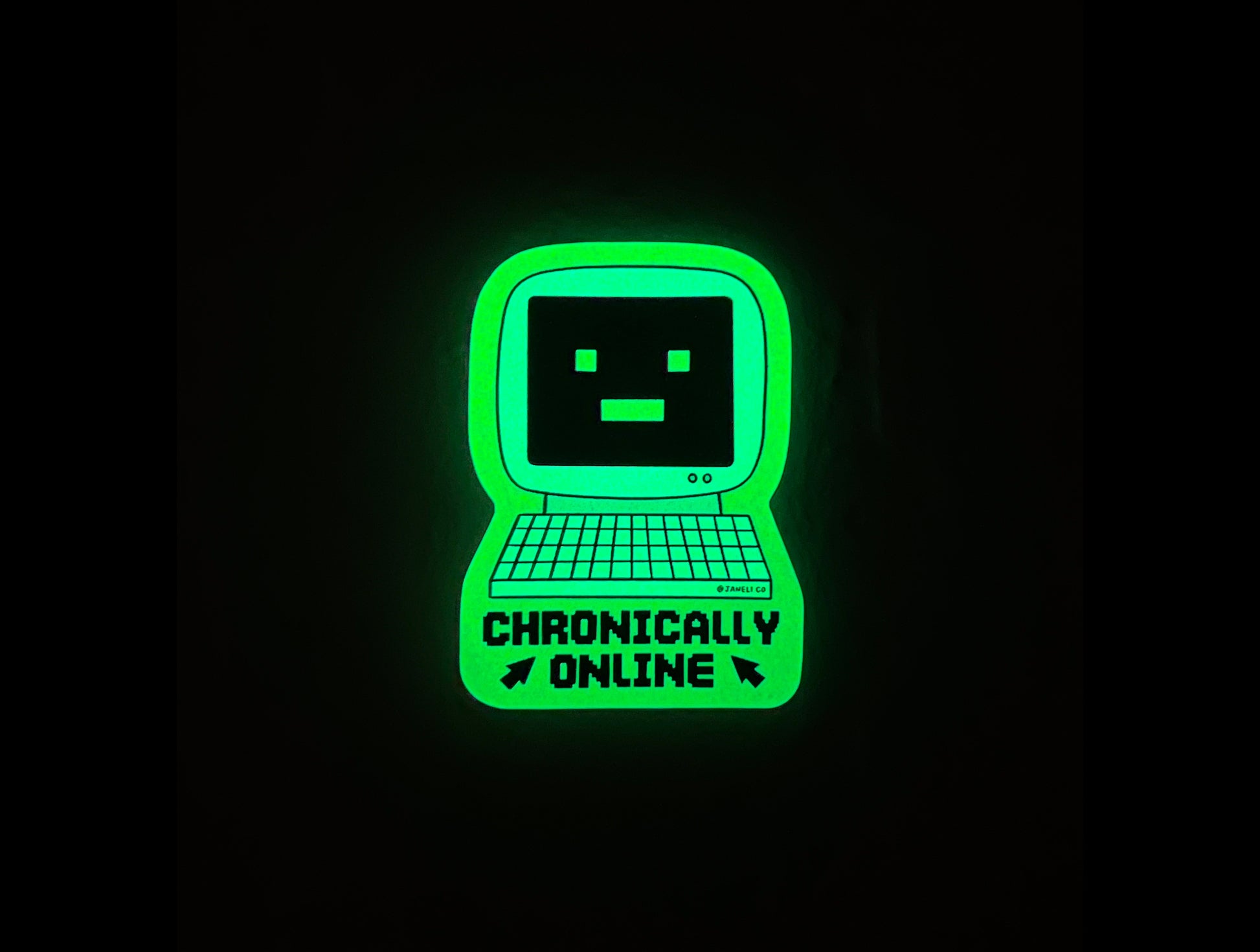 A glow in the dark sticker of a retro computer with a -_- face that says "Chronically Online" in the dark.