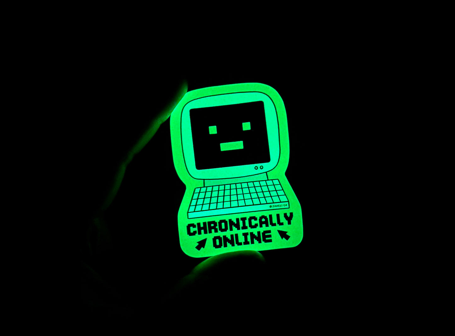 
A hand holding a glow in the dark sticker of a retro computer with a -_- face that says "Chronically Online" in the dark.
