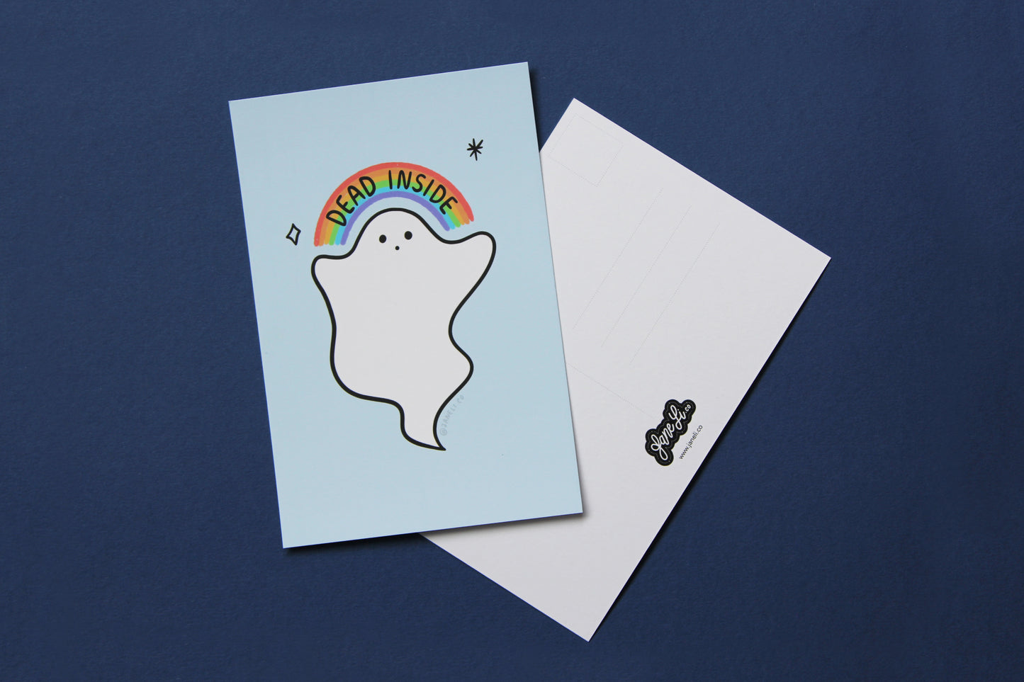 A JaneLi.Co mini print/postcard that shows a little white ghost holding up a rainbow that says "Dead Inside" and a back postcard side of the same print over a navy blue background.