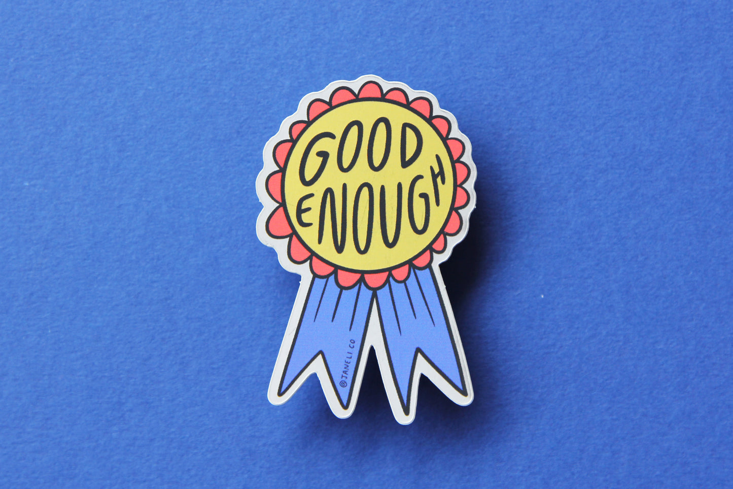 A JaneLi.Co sticker of a red and blue award ribbon that says "Good Enough" over a blue background.