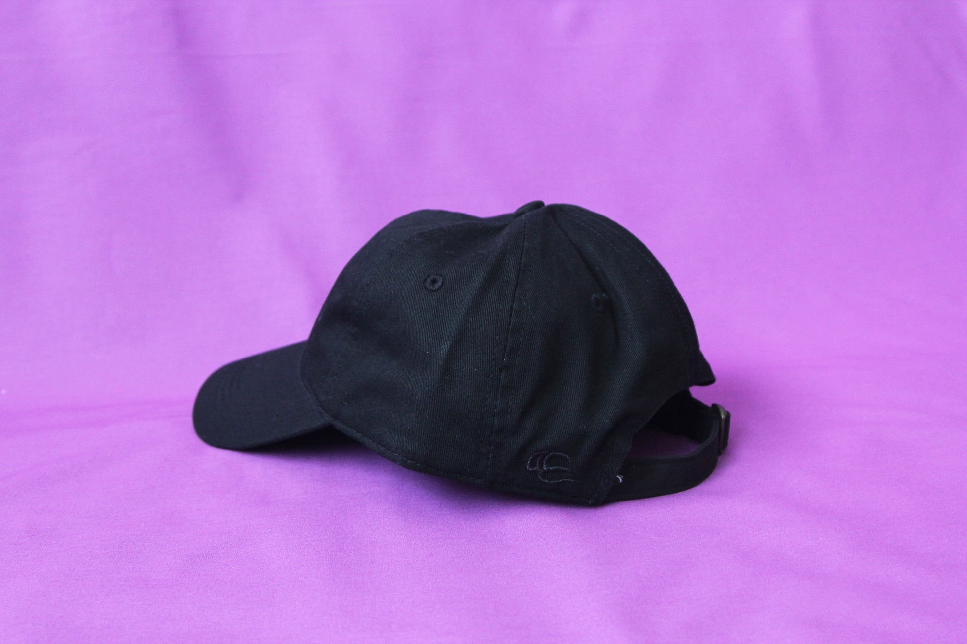 A photo of the back of a black dad hat with an adjustable buckle strap.