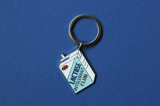 An enamel keychain showing a soymilk carton that says" Lactose Intolerant Club" over a blue background.