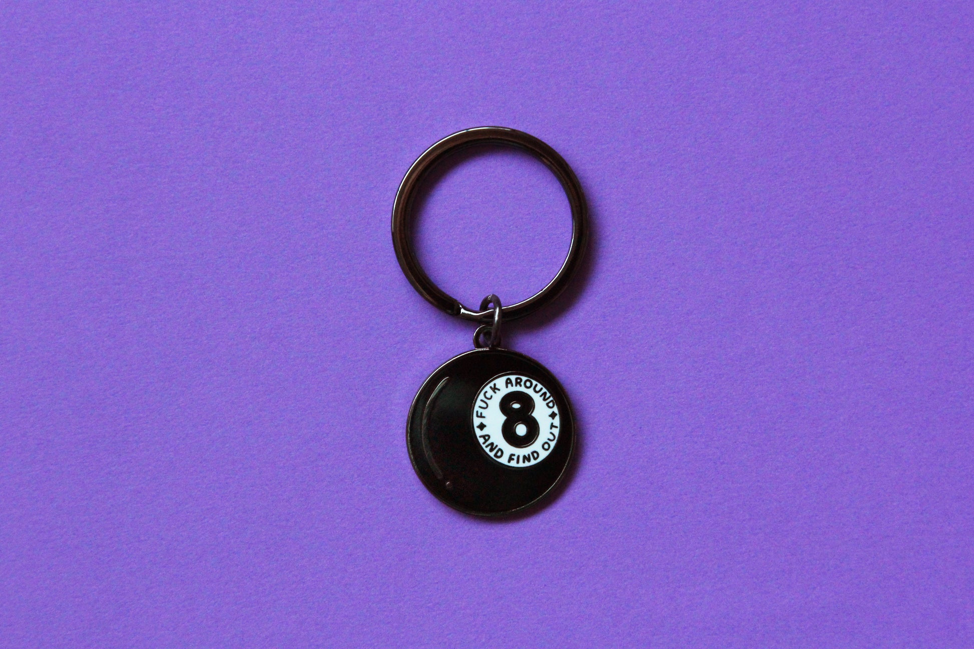 An enamel keychain showing a magic 8 ball that says "Fuck around and find out" over a purple background.