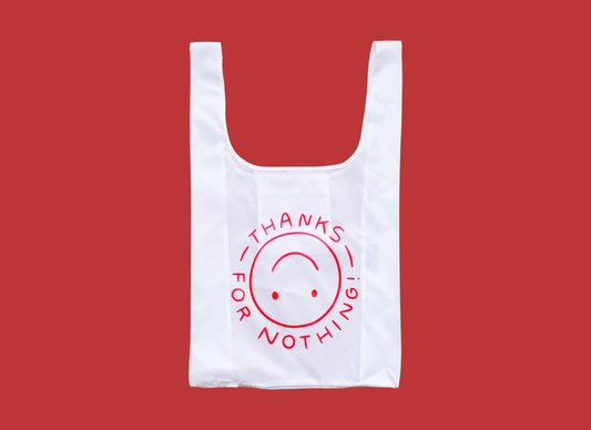 A photo of a white foldable grocery bag with an upside down smiley face that says "Thanks for nothing" over a red background.