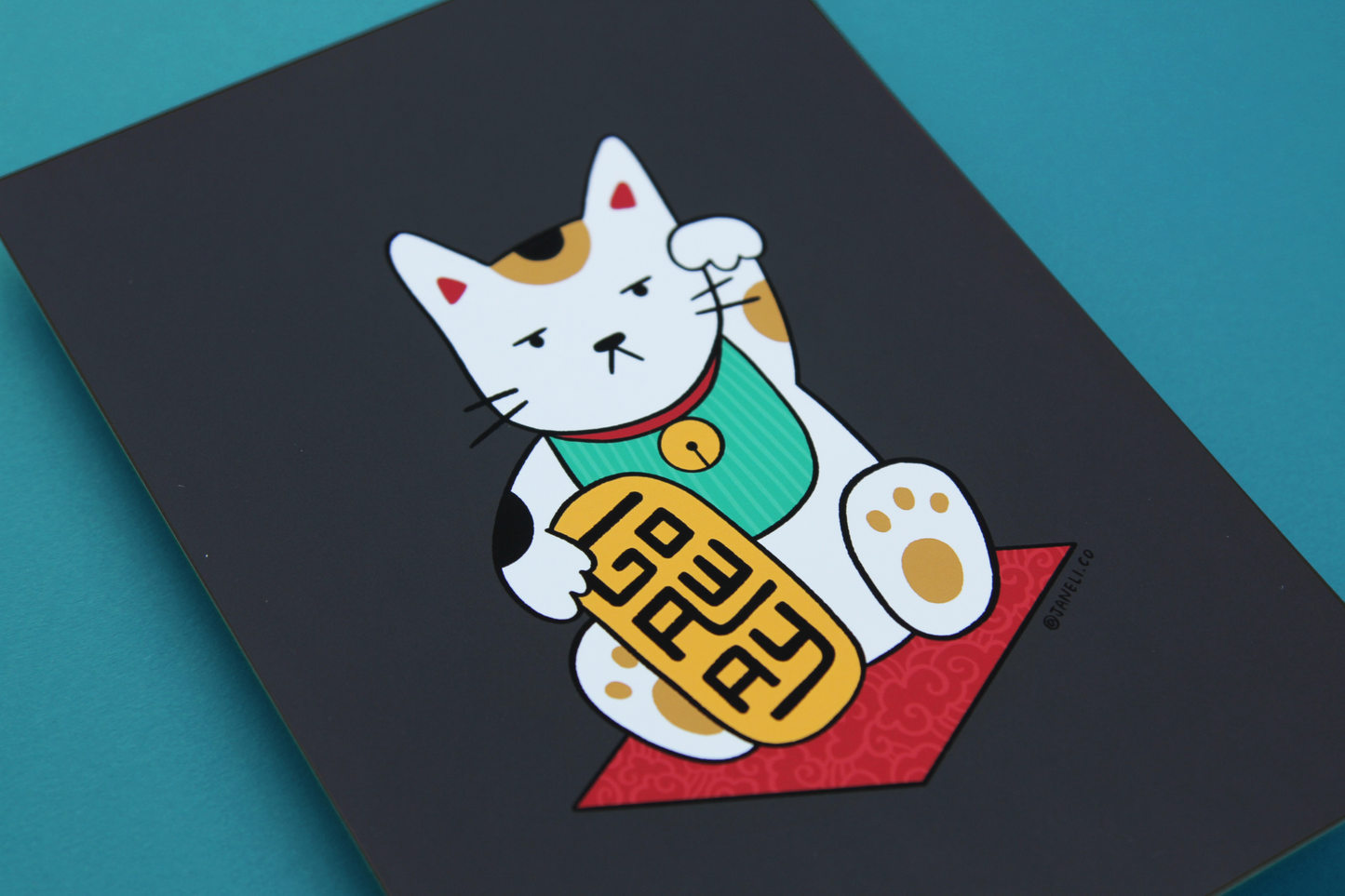 A close up of a JaneLi.Co print that shows a maneki neko cat holding a gold bar that says "Go Away" over a teal background.
