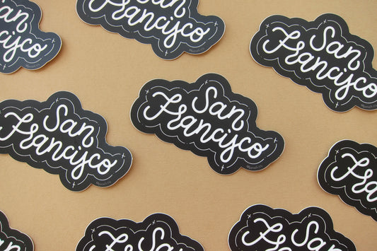 A grid of black and white JaneLi.Co stickers that say "San Francisco" in cursive lettering over a tan background. 
