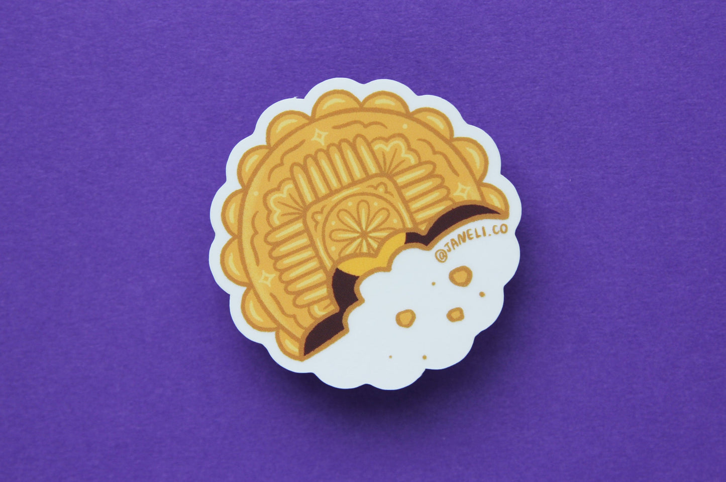 A JaneLi.Co sticker of a mooncake over a purple background. 