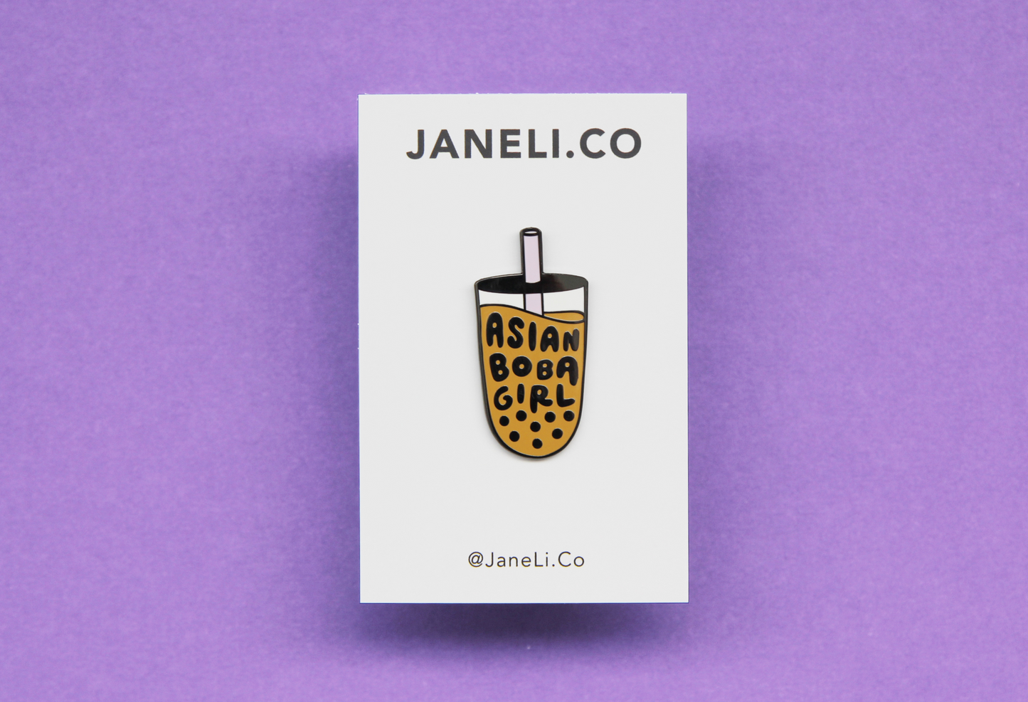 An enamel pin showing a mooncake with a bite out of it on a white JaneLi.Co backing card over a purple background.