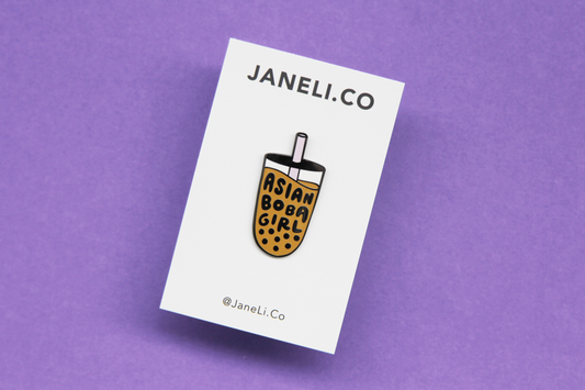 An enamel pin showing a cup of boba that says "Asian Boba Girl" with a purple straw on a white JaneLi.Co backing card over a purple background.