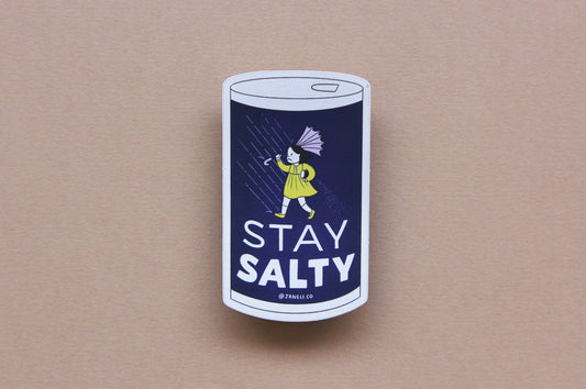 A JaneLi.Co sticker that says "Stay Salty" in the shape of a salt can with an angry salt girl holding an umbrella blow backwards from wind and rain over a navy blue background. 