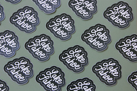 A grid of black and white JaneLi.Co stickers that say "Lake Tahoe" in cursive lettering over a green background. 