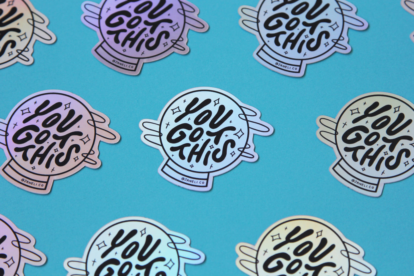 A grid of holographic JaneLi.Co stickers that say "You Got This" in a magic crystal ball over a blue background. 