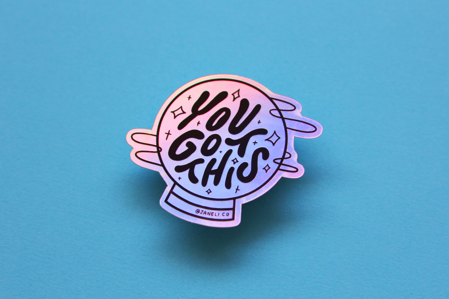 A holographic JaneLi.Co sticker that says "You Got This" in a magic crystal ball over a blue background. 