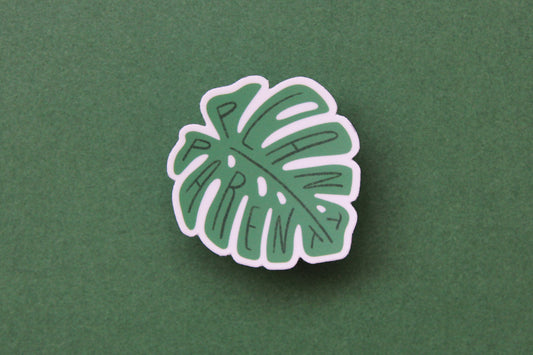 A green JaneLi.Co sticker that says "Plant Parent" in the shape of a monstera leaf over a green background. 