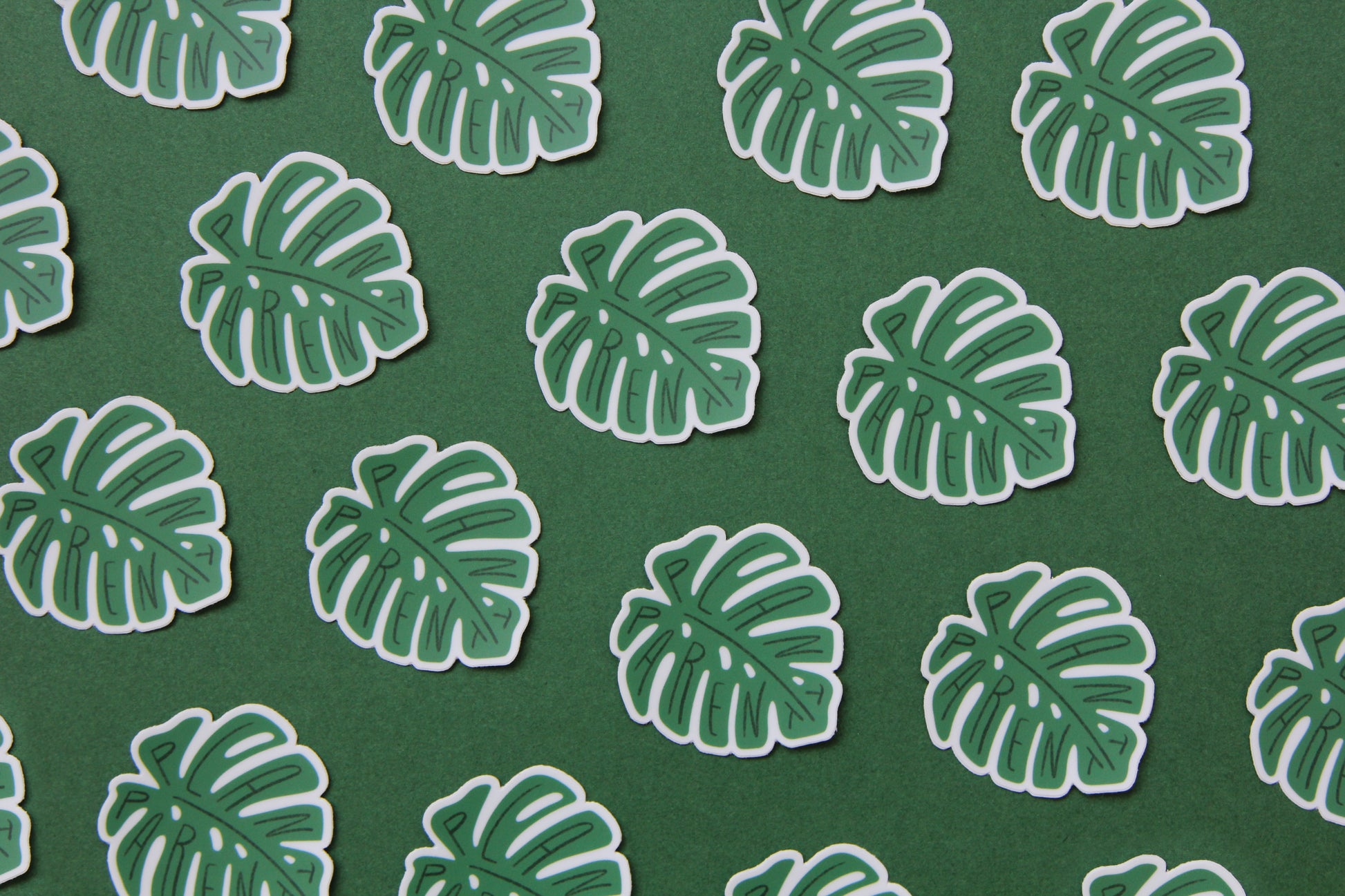 A grid of green JaneLi.Co stickers that say "Plant Parent" in the shape of monstera leaves over a green background. 