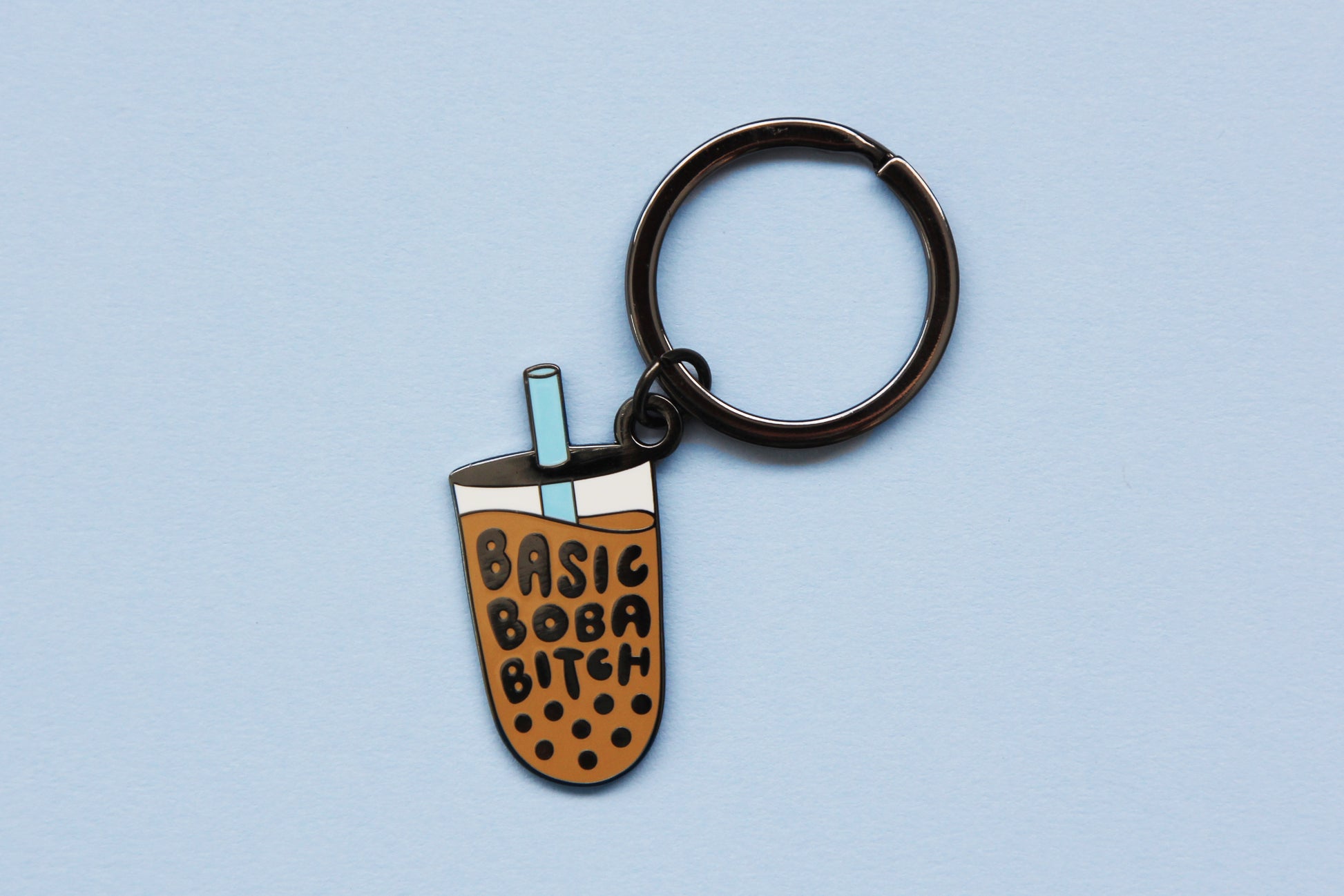 An enamel keychain showing a cup of boba that says "Basic Boba Bitch" with a blue straw over a blue background.