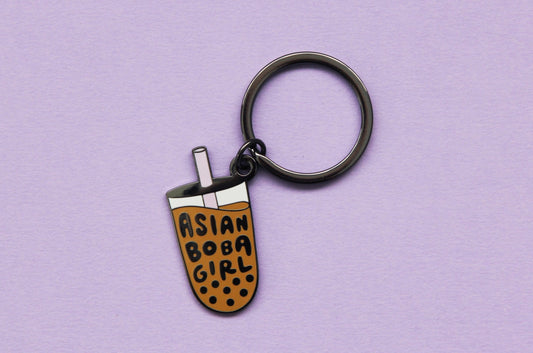 An enamel keychain showing a cup of boba that says "Asian Boba Girl" with a purple straw over a purple background.