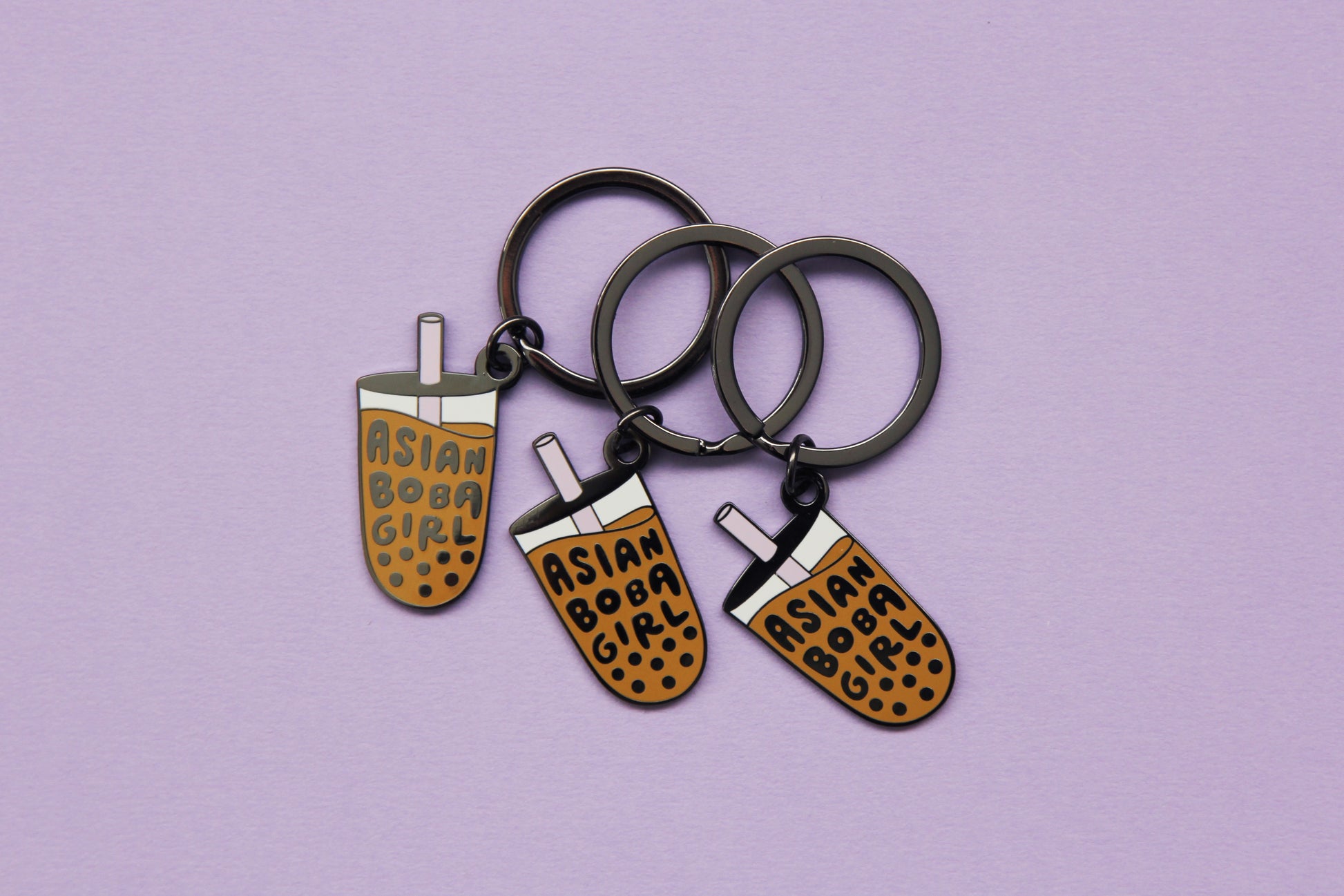 3 enamel keychains showing a cup of boba that says "Asian Boba Girl" with a purple straw over a purple background.
