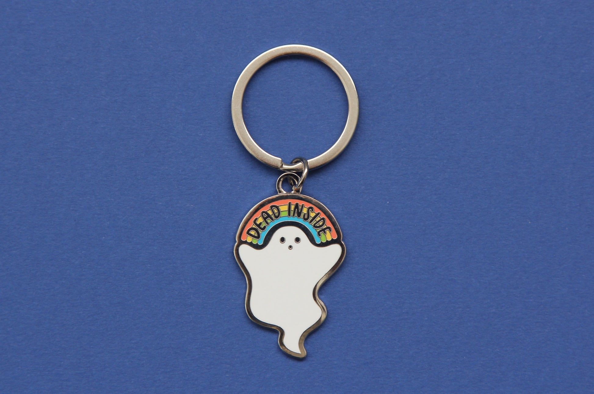 An enamel keychain showing a little white ghost holding a rainbow that says "Dead Inside" over a navy background.