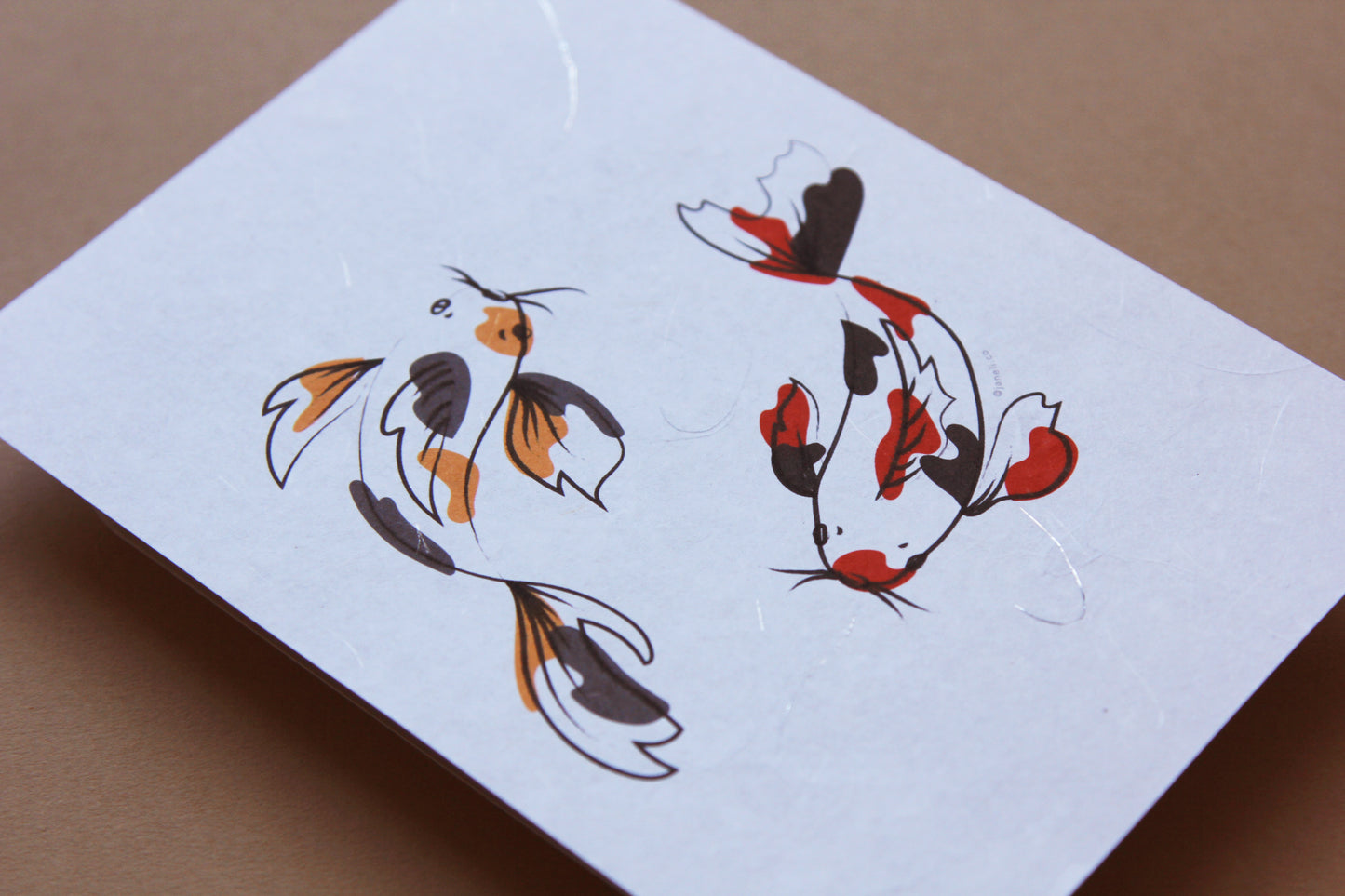 A close up of a JaneLi.Co print of 2 circling koi over a tan background.