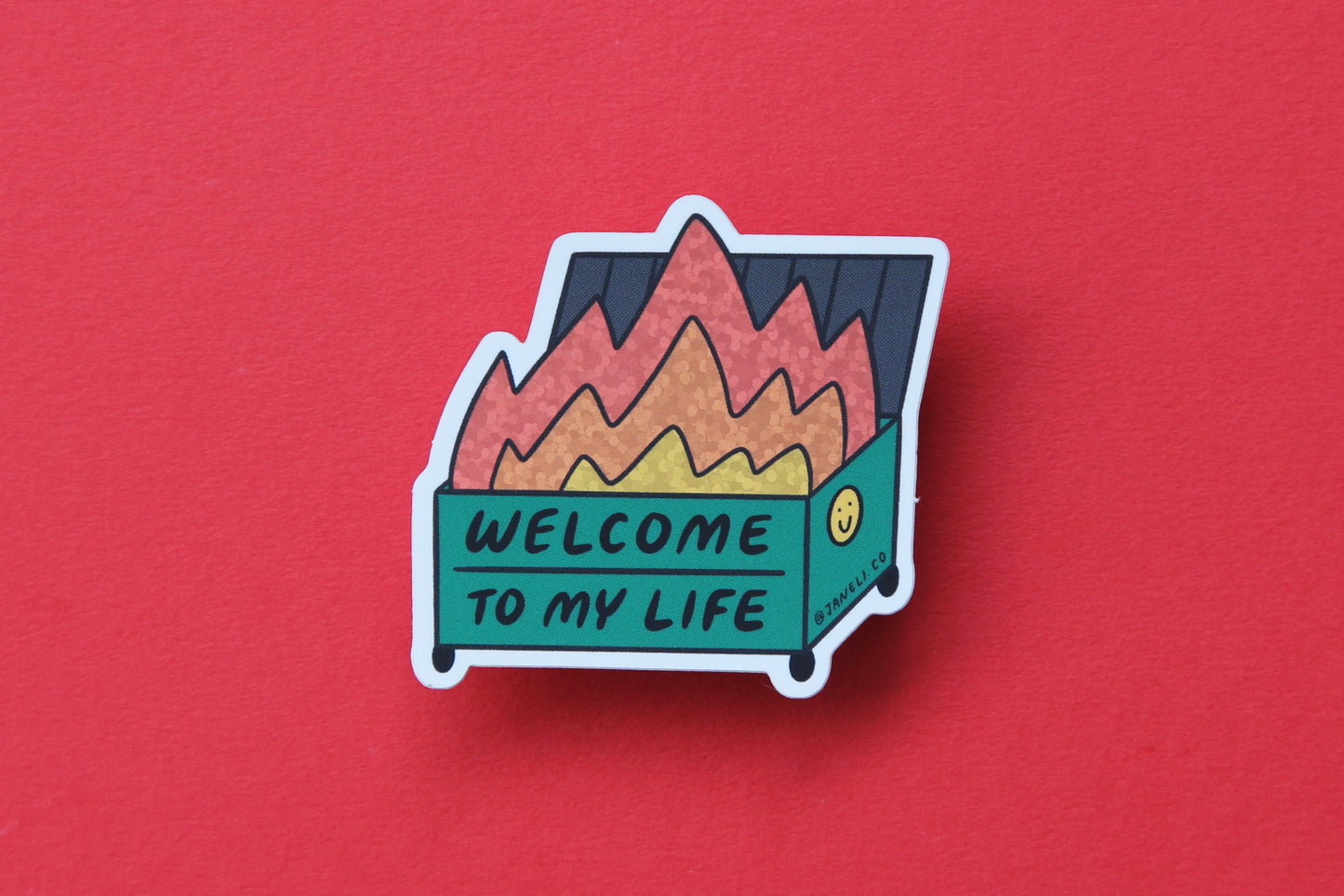 A JaneLi.Co sticker that says "Welcome to my life" in the shape of a dumpster on fire over a red background.