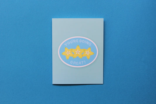 A photo of a blue greeting card with a sliced starfruit that says "You're doing great" on a blue background.