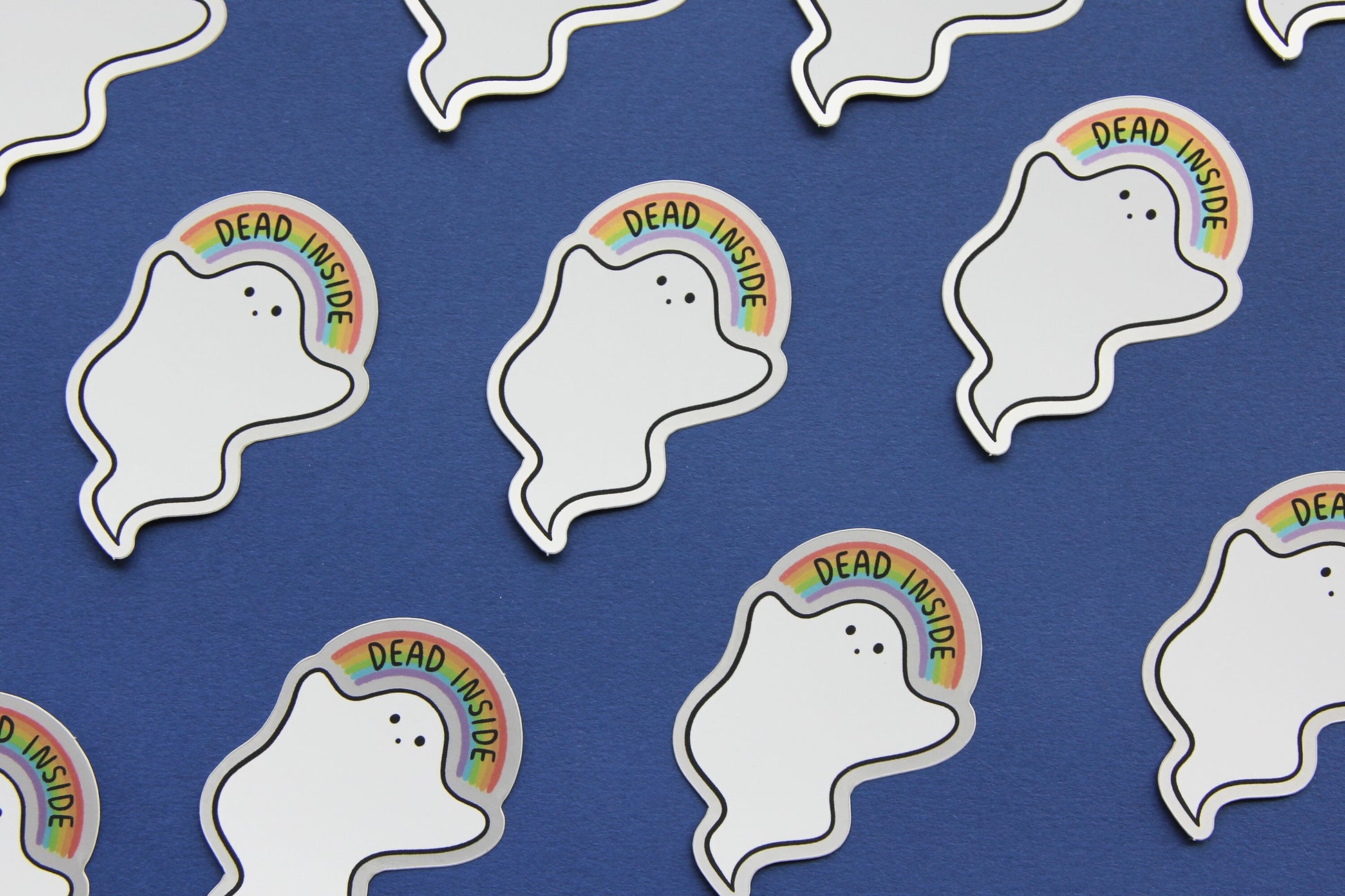 A grid JaneLi.Co stickers that show little white ghosts holding up rainbows that says "Dead Inside" over a navy blue background. Each sticker has a metallic silver border.